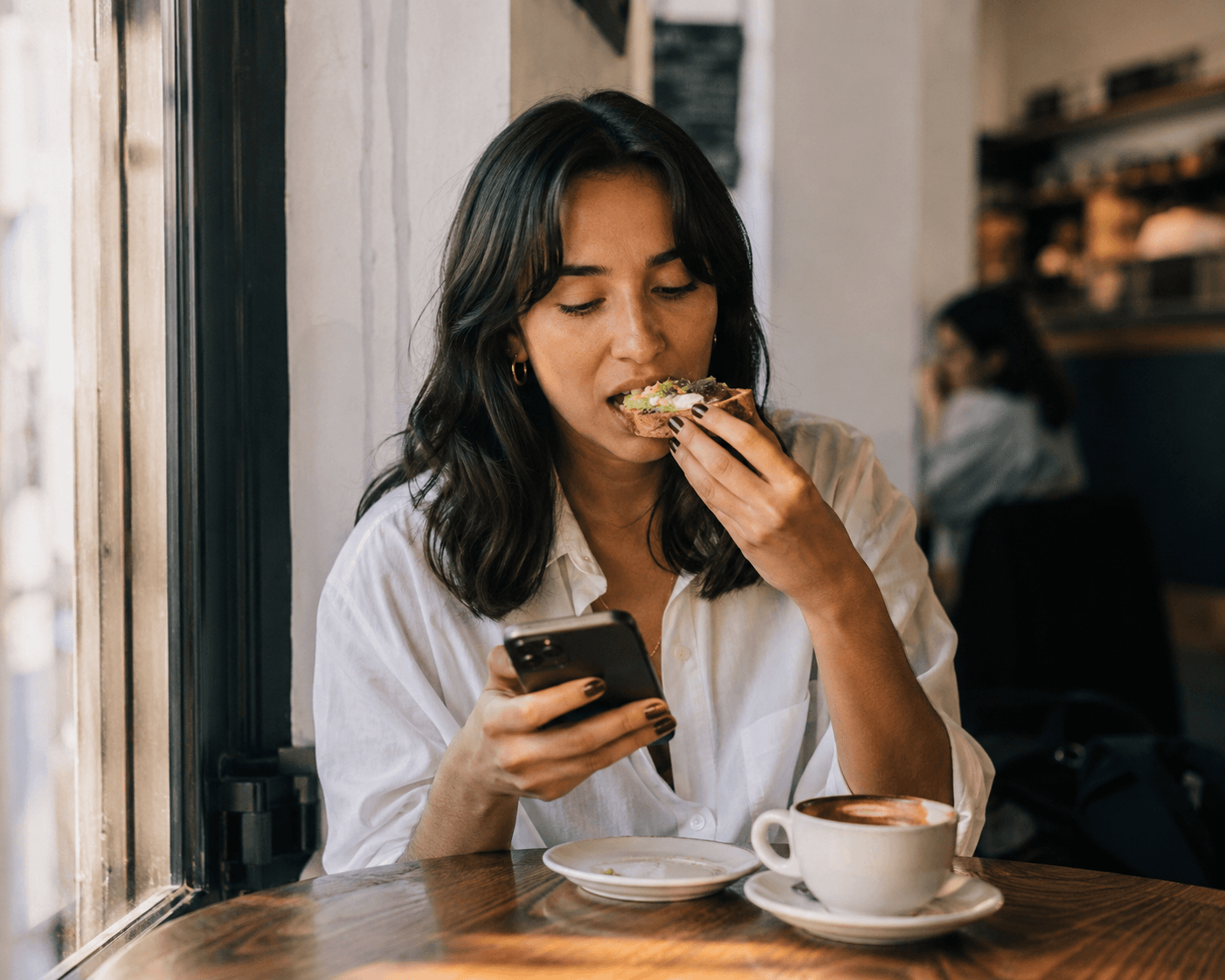 Someone glancing at their phone at a café, mid-bite (real, candid)
